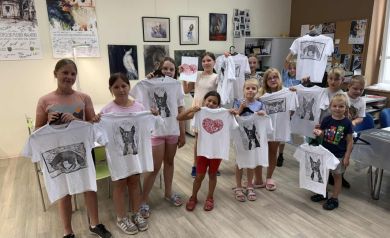 Grupka dzieci ustawiona do zdjęć z koszulkami wykonanymi podczas zajęć. 