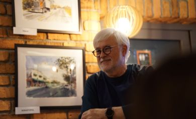 Uśmiechnięty i zadowolony artysta, w tle jego dzieła