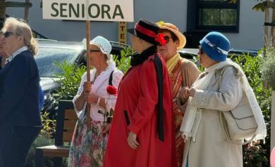 Grupka osób w kolorowych strojach z tabliczką z napisem ,,Klub aktywnego seniora'.