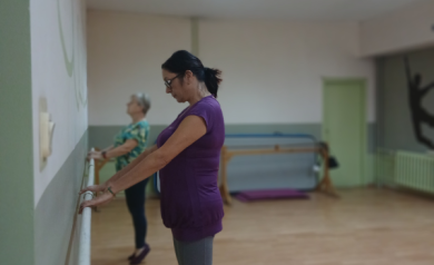 Uczestniczki zajęć wykonują ćwiczenie. Stoją na palcach i trzymają się drążka.