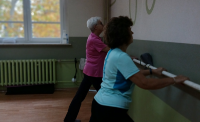 Dwie kobiety w różowej i niebieskiej koszulce przy drążku, wykonują ćwiczenia.