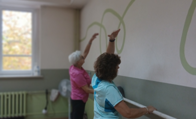 Kobieta w niebieskiej i kobieta w różowej bluzce wykonują ćwiczenie przy drążku.