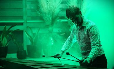 Muzyk grający na marimbie. Na kameralnej scenie dominuje przytulne zielone światło sceniczne.