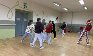 Zdjęcie przedstawia grupę młodych ludzi, dziewcząt, uczestniczących w zajęciach tanecznych w sali tanecznej. Jedna z kobiet ma na głowie świąteczną czapkę.