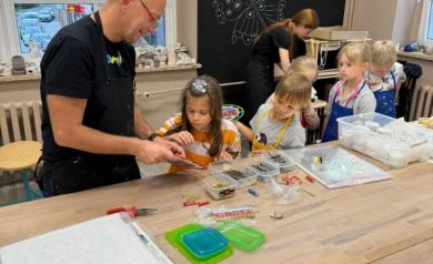 Na zdjęciu dzieci oraz prowadzący warsztaty podczas pracy nad zegarami. 
