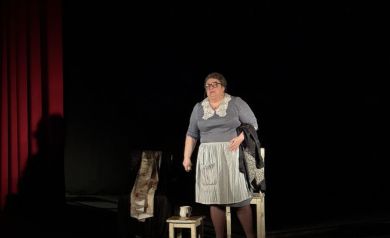 Na scenie kobieta - aktorka. Obok niej rekwizyty takie jak krzesło, mały stołeczek, szklanka. 