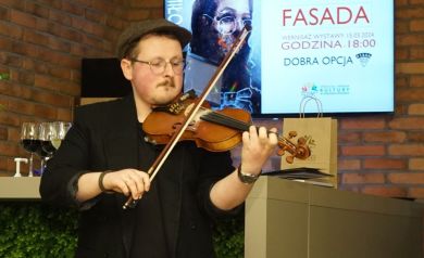 Mężczyzna elegancko ubrany, gra na skrzypcach, wykonuje swój występ na wernisażu wystawy FASADA