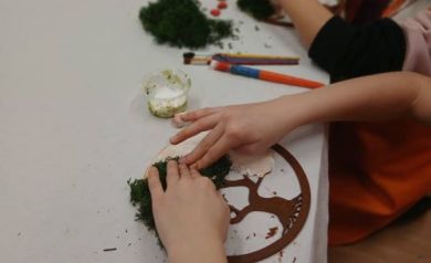 Na zdjęciu widać dłonie dzieci przyklejające mech do wykonywanych prac. 