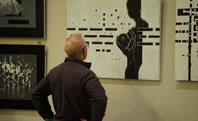 Mężczyzna w okularach stoi tyłem do aparatu i ogląda wiszące na ścianie zdjęcia. 