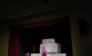 Na scenie aktorzy odgrywający scenę. 