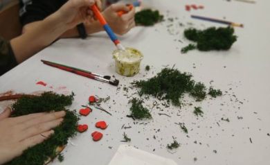 Zdjęcie przedstawia akcesoria potrzebne do wytworzenia ,,Drzewek życia', zaś w tle widać pracujące dzieci nad swoimi pracami. 