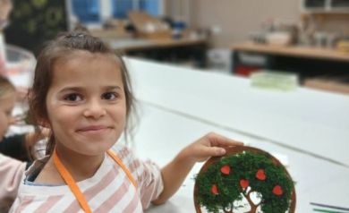 Na zdjęciu dziewczynka w pomarańczowym fartuszku prezentująca swoja pracę. 