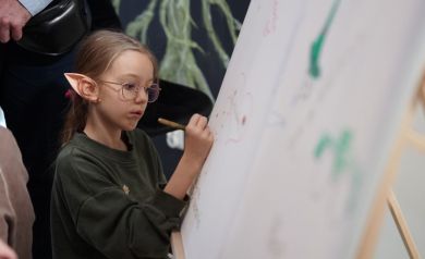 Dziewczynka w okularach pisze markerem po płótnie.