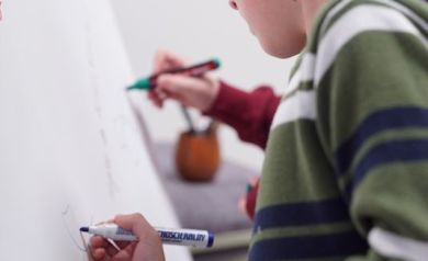 Chłopiec w pasiastym swetrze maluje markerem po płótnie.