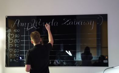 Młody mężczyzna piszący białym markerem po czarnej tablicy.