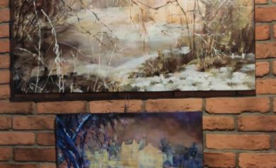 Na zdjęciu dwa obrazy wiszące na ceglastej ścianie. Obrazy przedstawiają roślinność i budynki. 