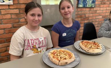 Dwie dziewczyny, przed nimi talerze z pizzą