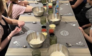 Składniki do pizzy na stole, przy nich siedzą dziewczyny