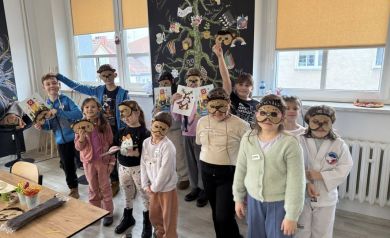 Grupa dzieci pokazująca swoje prace plastyczne w maskach na oczy