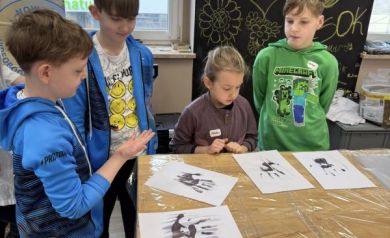 Chłopcy patrzący na kartki papieru, na których odbili swoje dłonie