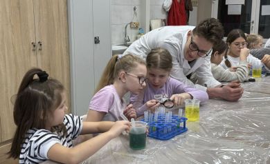 Pan pochylający się nad dziewczynkami robiącymi eksperyment