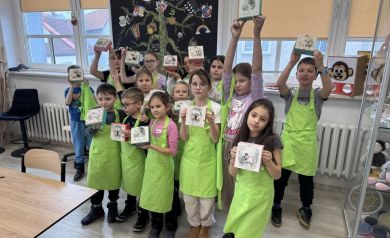 Grupa dzieci w zielonych fartuszkach pokazująca swoje drewniane pudełeczka