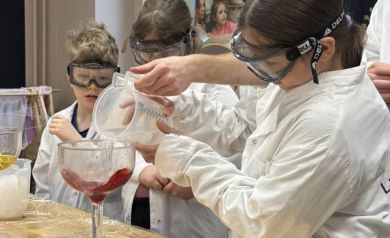 Grupa dzieci patrzy na eksperyment w dużym, szklanym kielichu