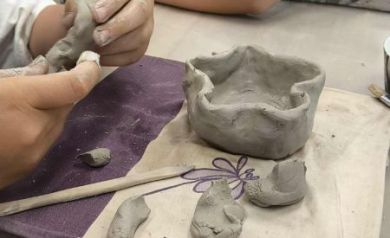 Na pierwszym planie praca wykonana na warsztatach ceramicznych. W tle widać dzieci biorące udział w zajęciach. 