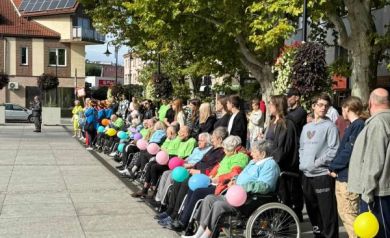 Uczestnicy wydarzenia, niektórzy poruszający się na wózkach inwalidzkich. Trzymają w dłoniach kolorowe balony.