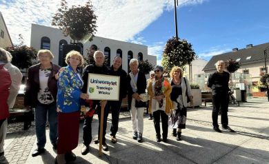 Grupka osób z tabliczką, na której widnieje napis UNIWERSYTT TRZECIEGO WIEKU.