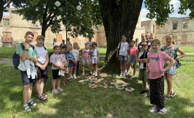 Dzieci ustawiające się do zdjęcia. Stoją przy drzewie. Z tyłu widać ruiny zamku. 