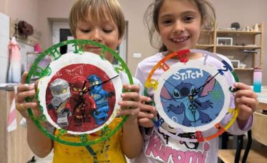 Dwójka dzieci prezentująca wykonane przez siebie zegary. 