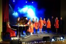 KONCERT. DZIECI ŚPIEWAJĄ, PO LEWEJ KOBIETA GRAJĄCA NA PIANINIE