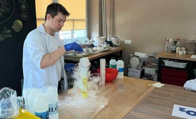 Mężczyzna przeprowadzający warsztaty chemiczne. Wokół niego różne akcesoria do przeprowadzania warsztatów. 
. 