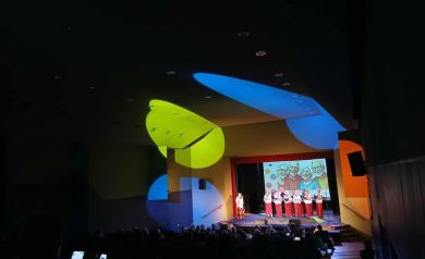 Na scenie występ zespołu śpiewaczego. Na pierwszym planie widać publiczność.