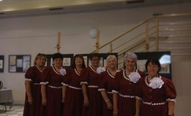 Na zdjęciu zespół śpiewaczy pozuje do zdjęcia. Kobiety ubrane są w czerwone suknie z białymi dodatkami.