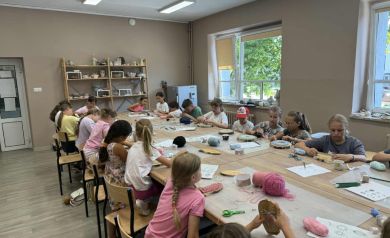 Dzieci biorące udział w warsztatach string art siedzą przy stole, na którym znajdują się potrzebne materiały do przeprowadzenia takich zajęć. 