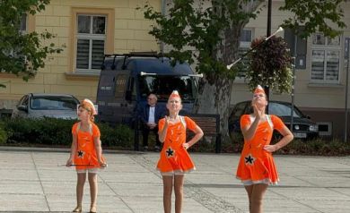 Trzy mażoretki ubrane w pomarańczowe stroje podczas swojego występu.