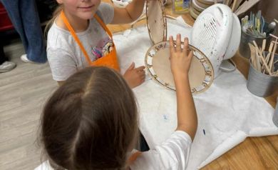 Dzieci suszące swoje zegary przy sprzęcie do tego przeznaczonym. Widać tam również inne przyrządy do tworzenia rękodzieła. 