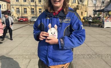 Uśmiechnięty chłopak w niebieskiej kurtce, trzyma w dłoni znalezioną torebkę niespodziankę w kształcie zajączka.