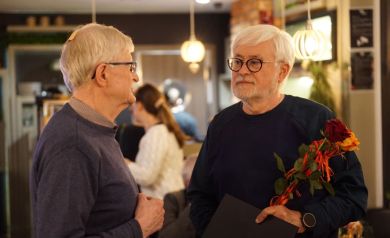 Artysta rozmawia z innym mężczyzną, trzymając w ręku różę