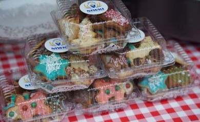 Na zdjęciu pudełka z pierniczkami świątecznymi z naklejkami Koła Gospodyń Wiejskich z Niwek. Pudełka ustawione są w piramidę na biało-czerwonym obrusie w kratkę. 