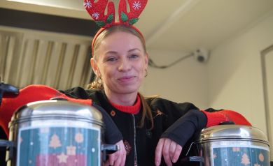 Na zdjęciu kobieta z założonymi na głowie czerwonymi rogami renifera. Opiera się o dwa termosy. 