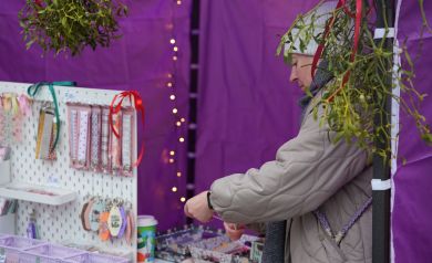 Kobieta sprzedająca zakładki podczas jarmarku. Widać namiot ozdobiony jemiołą. 
