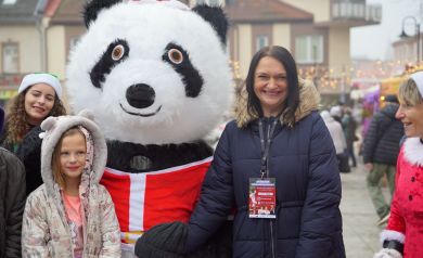 Kobiety i dziewczynka pozują do zdjęcia z dużą maskotką pandy. 