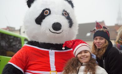 Dwie młode kobiety w ozdobach świątecznych na głowach pozują do zdjęcia z dużą maskotką pandy. 