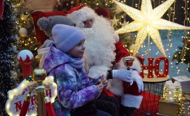 Dwójka dzieci z mężczyzną w stroju Mikołaja w świątecznie przystrojonym namiocie. 