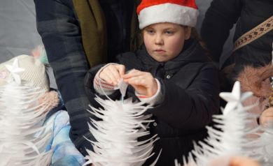 Dziewczynka w świątecznej czapce wykonuje choinkę podczas warsztatów. 