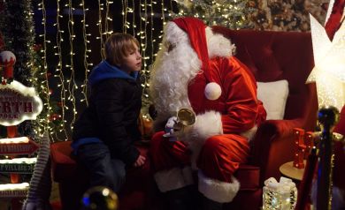 Chłopiec rozmawiający z mężczyzną przebranym za Mikołaja, znajdują się w namiocie przystrojonym w świąteczne dekoracje.