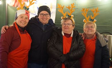 Na zdjęciu trzy kobiety z założonymi na głowach ozdobnymi rogami renifera. Wśród kobiet stoi równie mężczyzna w okularach. Wszyscy uśmiechają się do zdjęcia. 